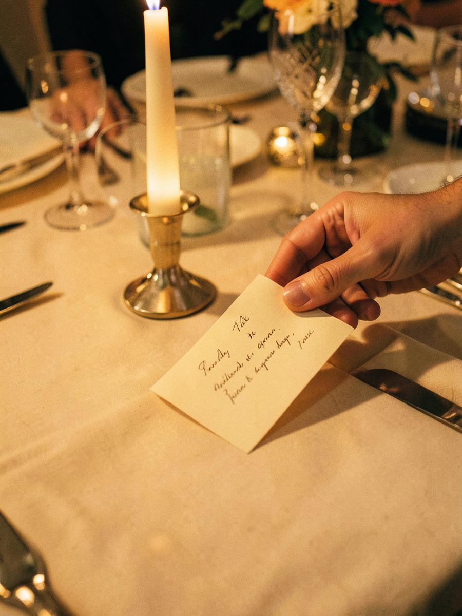 A hand placing a handwritten place card beside a candle at a dinner